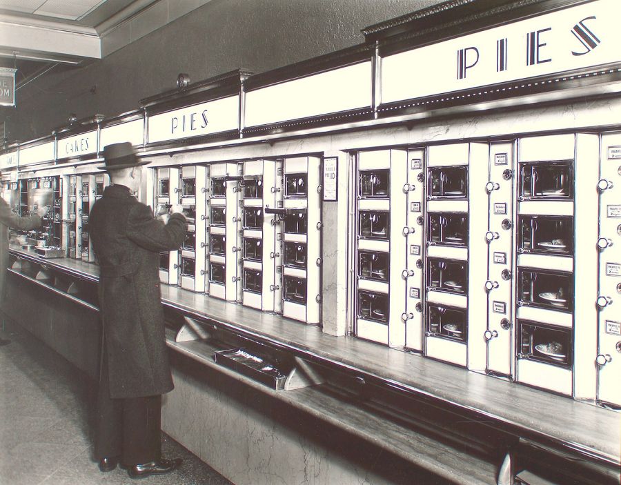 Restauracja Horn & Hardart Automat, USA, 1902. Pierwsza restauracja w pełni obsługiwana przez automaty vendingowe wydające posiłki. W automatach klienci mogli kupić ciasto, pieczeń i inne dania przez okienka. Za kulisami kuchnia pełna personelu przygotowywała jedzenie i uzupełniała puste miejsca w maszynie. Źródło: Biblioteka Publiczna w Nowym Jorku